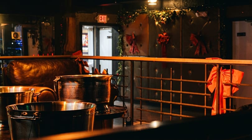 Dark, festive bar interior with metal ice buckets, leather seating, and holiday decorations.