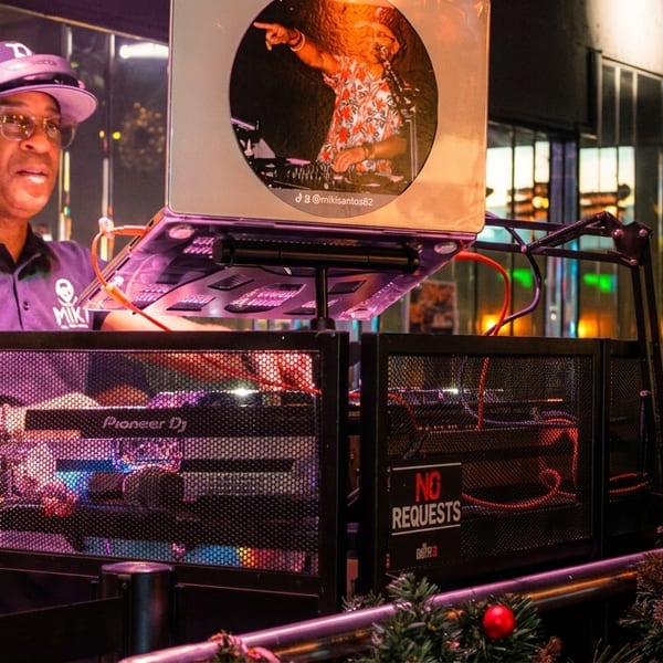 A DJ in a purple polo shirt and headphones plays music at a Pioneer DJ setup.