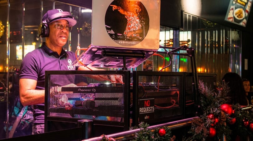 A DJ in a purple polo shirt and headphones plays music at a Pioneer DJ setup.