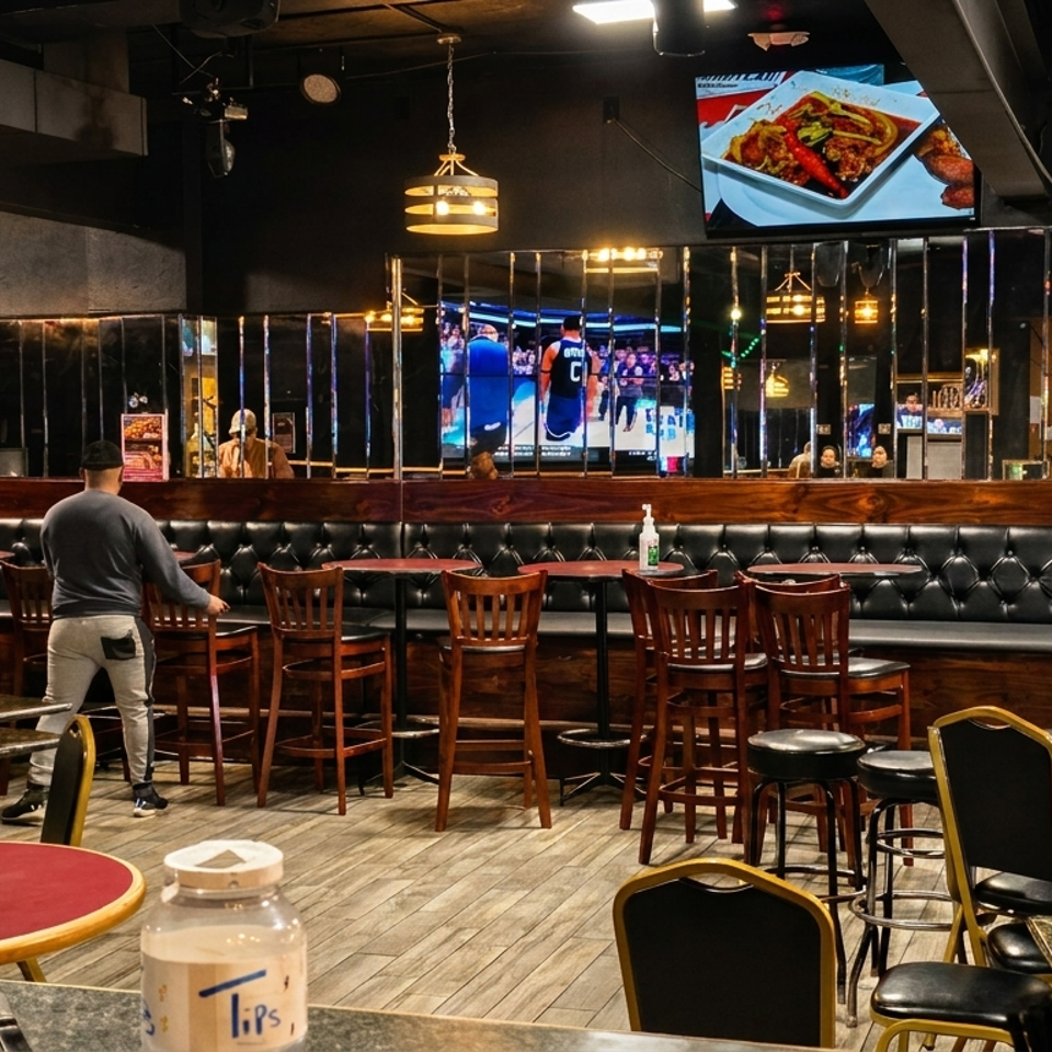 Two men arrange chairs and tables in a restaurant with dark decor, TVs, and a Corona Extra cutout.
