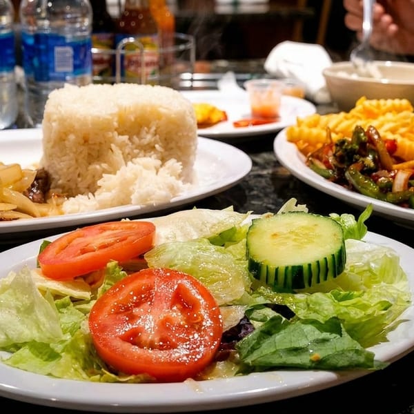 Plates of stir-fried beef and onions, rice, salad, and waffle fries on a dark table.